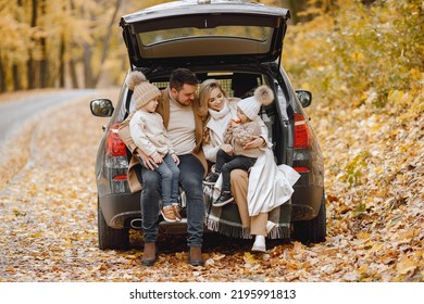 Young Family Sitting At Open Trunk Of Hatchback Car In Autumn Forest