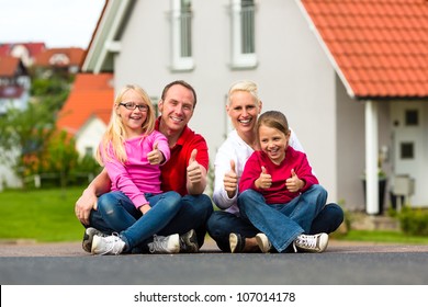 Young family sitting in the sun in front of their new home giving thumbs up
