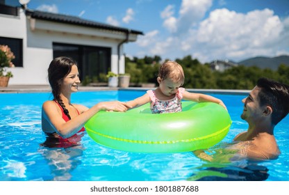 Young Family With Small Daughter In Swimming Pool Outdoors In Backyard Garden.