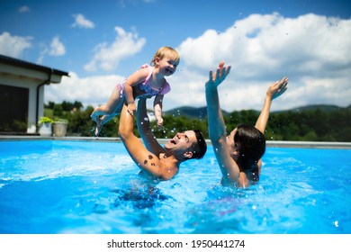 Young family with small daughter in swimming pool outdoors in backyard garden, playing.
