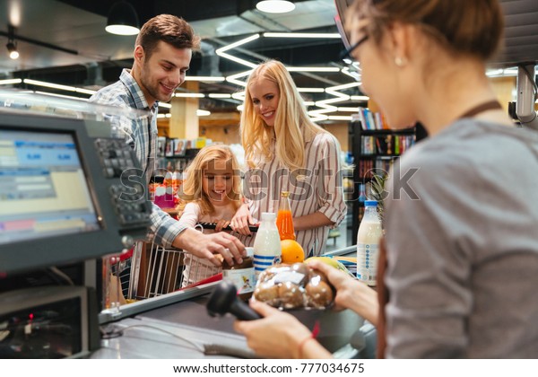 Young family standing at the cash counter\
buying groceries at the\
supermarket