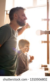 Young Family Standing In Front Of Mirror With Bulbs And Brushing Teeth In Bathroom, Morning Routine Concept