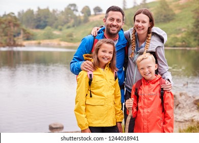 Young Family Standing On The Shore Of A Lake In The Countryside Looking To Camera Smiling, Lake District, UK