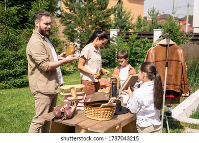 Young Family Standing At Table With Antique Things And Discussing What To Buy At Yard Sale