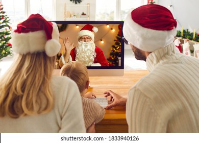 Young Family Staying At Home On Christmas Holidays And Having Online Lockdown Party. Mom, Dad And Son Looking At Computer Screen During Video Call With Santa Claus Who's Waving Hand To Greet Them