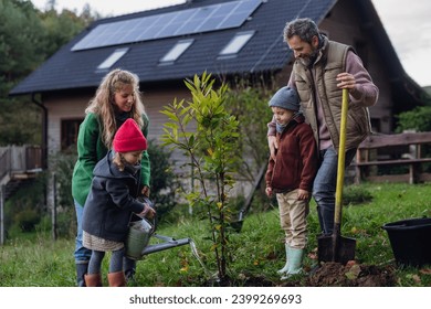 Young family taking care of home garden, planting tree. Mother, father and kids spending time outdoors during cold spring day. - Powered by Shutterstock