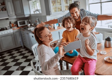 Young family taking a selfie on a smartphone while having breakfast and being messy in the kitchen - Powered by Shutterstock