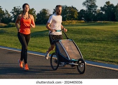 Young family with their child in a jogging stroller during jogging in a park. Active family running