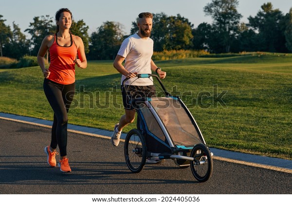 Young family with their child\
in a jogging stroller during jogging in a park. Active family\
running