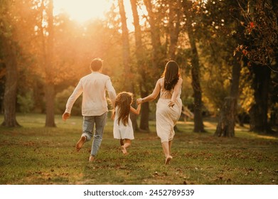 Young family of three are holding hands and running barefoot in park together. - Powered by Shutterstock