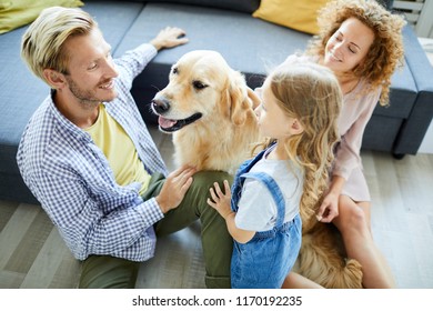 Junge Familie von drei Personen, die auf dem Boden mit Sofa sitzen, mit Haustier sprechen und spielen