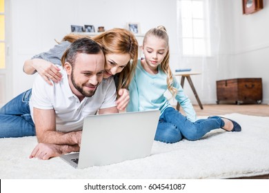 Young Family Of Three Using Laptop While Lying On Carpet At Home