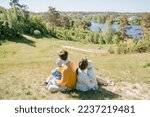 Young family with two children sits on a green hill and looks at the panoramic view of the countryside, the concept of a dream of living in a big country house