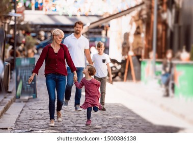 Young Family With Two Small Children Walking Outdoors In Town On Holiday.