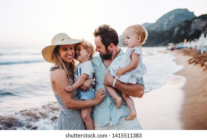 A Young Family With Two Toddler Children Standing On Beach On Summer Holiday.