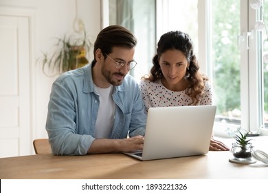 Young Family Using Laptop Together, Sitting At Wooden Table In Kitchen, Attractive Woman And Smiling Man Wearing Glasses Surfing Internet, Shopping Online, Making Purchases, Booking Tickets