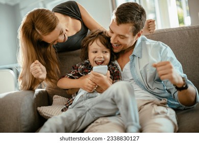 Young family using a smart phone while sitting on the couch in the living room - Powered by Shutterstock