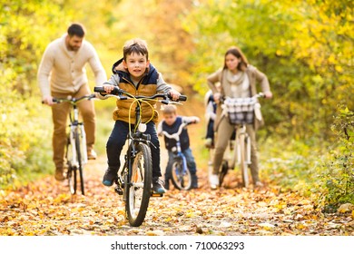 Young Family In Warm Clothes Cycling In Autumn Park