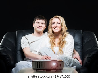 Young Family Watching A Movie Or A Sport Broadcast On A Laser Projector Sitting On A Sofa 