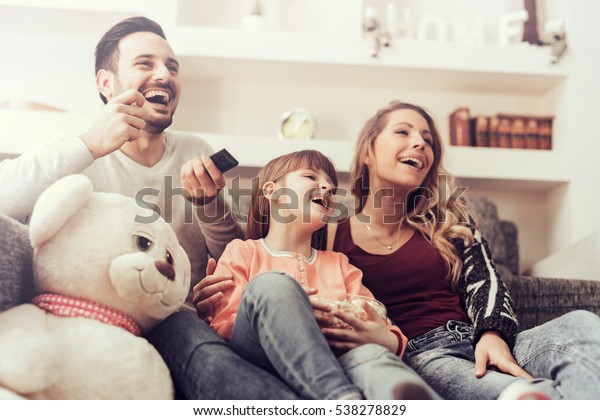 Young family watching TV together at home and\
having fun together.