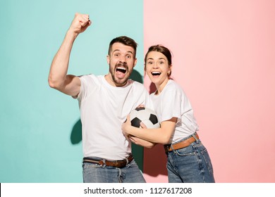 The Young Fans Celebrating On Blue And Pink Trendy Color Studio Background. The Young Man And Girl As Winners. Fan, Football, Soccer, Support Concept. Human Emotions Concept. Couple Are Happy