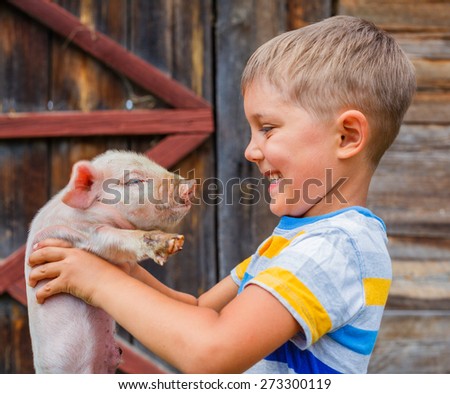 Young farmer - cute boy holding white piglet on a farm