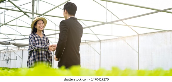 Young farmer pretty Asian girl shaking hand with businessman in the hydroponics vegetable organic green house farm. Successful of agriculture deal in business agreement. Seen in banner size.