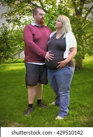 Young Farmer's Couple Together On Garden. Pregnant Mother And Overweight Father. People Working And Enjoying Life On Countryside. Pregnancy And Parenting.