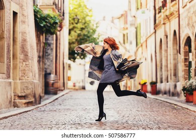 Young Fashion 20 Year Old Girl With Red Hair Running Down The Street, Wearing Light Dress, Black Tights, High Heel Shoes And Warm Plaid Jacket