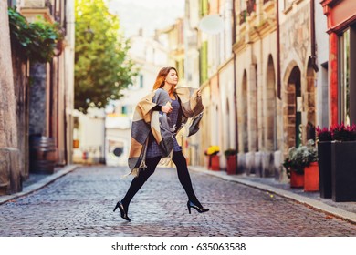 Young Fashion 20 Year Old Girl With Red Hair Running Down The Street, Wearing Light Dress, Black Tights, High Heel Shoes And Warm Plaid Jacket