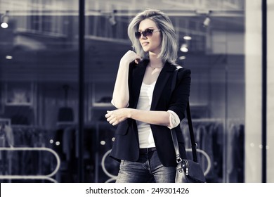 Young Fashion Blond Business Woman With Handbag In Black Blazer And Sunglasses Walking On City Street 