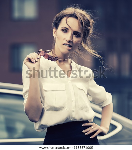 Young\
fashion business woman next to her car  Stylish female model with\
bun updo hair wearing white shirt and pencil\
skirt