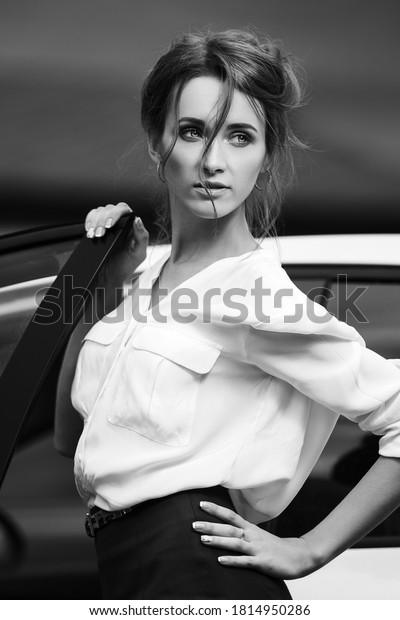 Young\
fashion business woman next to her car  Stylish female model with\
bun up do hair in white shirt and pencil\
skirt