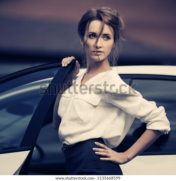 Young\
fashion business woman outside her car  Stylish female model with\
bun updo hair wearing white shirt and pencil\
skirt