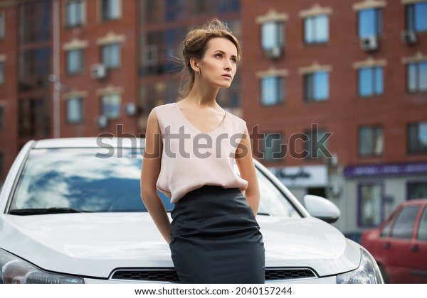Young fashion business woman outside her car \
Stylish female model with bun updo hair in pink sleeveless blouse\
and black pencil skirt