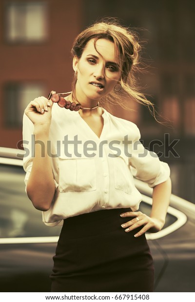 Young\
fashion business woman standing in a city street beside her car.\
Stylish female model in white blouse\
outdoor