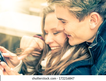 Young fashion couple of lovers playing with mobile smart phone outdoors - Relationship love concept with happy boyfriend and girlfriend together having fun at first date - Desaturated retro filter - Powered by Shutterstock