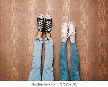 Young Fashion Couple's Legs In Jeans And Sneakers Feet Up On Wall