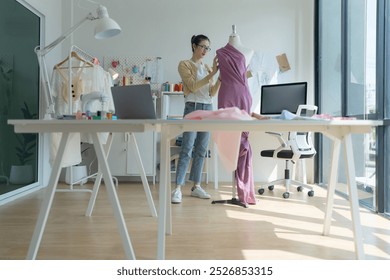 Young fashion designer is working in her bright studio, marking fabric for cutting. She is surrounded by mannequins, clothes and a sewing machine - Powered by Shutterstock