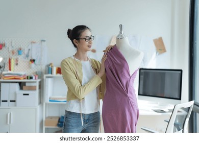 Young fashion designer is working in her bright studio, marking fabric for cutting. She is surrounded by mannequins, clothes and a sewing machine - Powered by Shutterstock