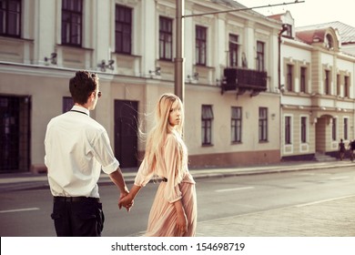 Young Fashion Elegant Stylish Couple Posing On Streets Of European City In Summer Evening Weather. Sensual Blonde Vogue Girl With Handsome Hipster Man Walk On The Road In Europe