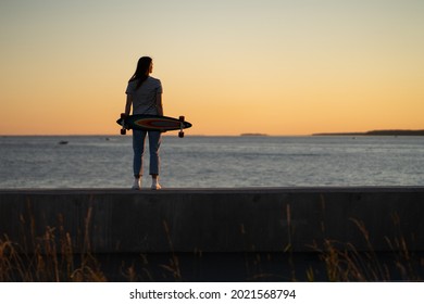 Young fashion girl with longboard enjoy sunset looking at seaside skyline. Stylish trendy female longboarder silhouette over beautiful setting sun at sea coast. Freedom, youth and lifestyle concept - Powered by Shutterstock