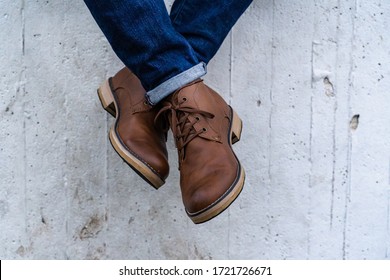 Young fashion man in blue jeans and brown boots next to a wall