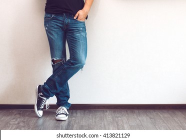 Ноги молодого модного мужчины в джинсах и кроссовках на деревянном полу