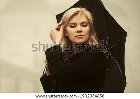 Young fashion woman with umbrella walking in a fog Stylish female model in classic black coat and dark purple scarf