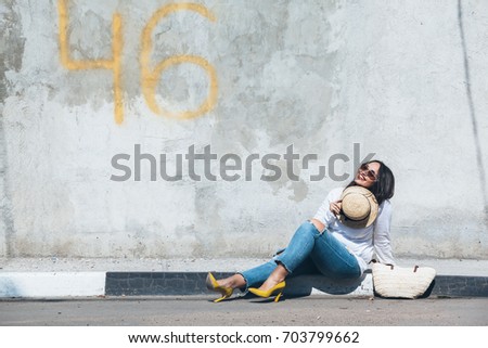 Young fashion woman wearing ripped jeans, colorful heel shoes and straw accessories posing over gray concrete city wall. Plus size model.