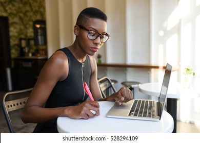 Young Fashionable African Business Woman Working Hard At The Cafe On The Laptop, Making Notes