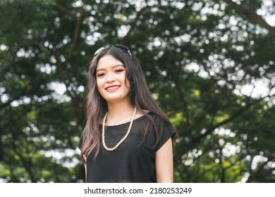 A Young Fashionable Asian Lady In A Black Top And Pearl Necklace. A Rich Kid Smiling.