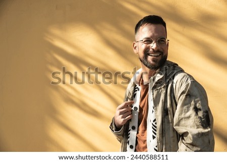 Young fashionable hipster man posing outdoor with yellow wall background. Style and independence millennial male standing for portrait. World traveler youth culture