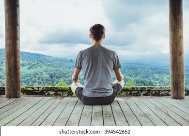 Young fashionable man meditating in the gazebo on the background of the mountains in Bali